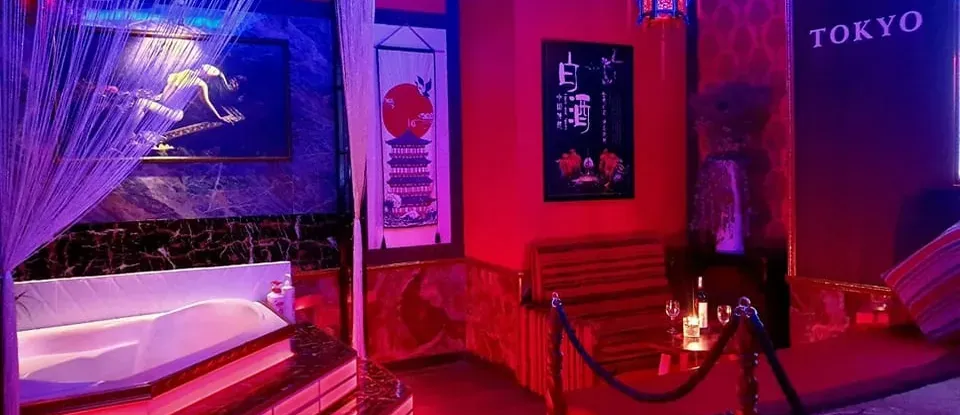 붉은 조명 아래 자쿠지와 침대가 있는 일본풍 마사지실
